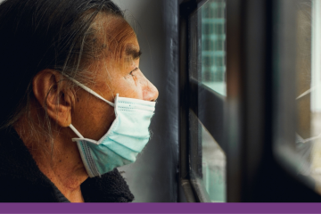 Older man looking outside of a window wearing a face mask